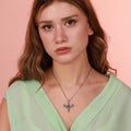 Woman wearing a green top and a necklace with a dragonfly pendant against a pink background
