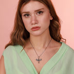 Woman wearing a green top and a necklace with a dragonfly pendant against a pink background