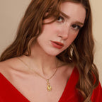 Woman wearing a gold necklace with a pendant against a beige background