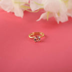 Gold ring with a red gemstone on a pink background with white flowers.