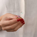 Hand holding a ring with a pink gemstone against a plain background