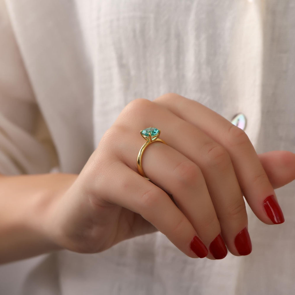 Hand wearing a gold ring with a green gemstone against a white background