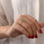 Hand wearing a gold ring with a green gemstone against a white background