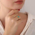 Close-up of a hand wearing a gold ring with a green gemstone, against a neutral background.