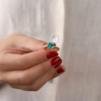 Hand holding a ring with a blue gemstone against a plain background