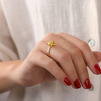 Hand wearing a gold ring with a red nail polish against a white background