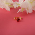 Gold ring with a red gemstone on a pink background with white flowers