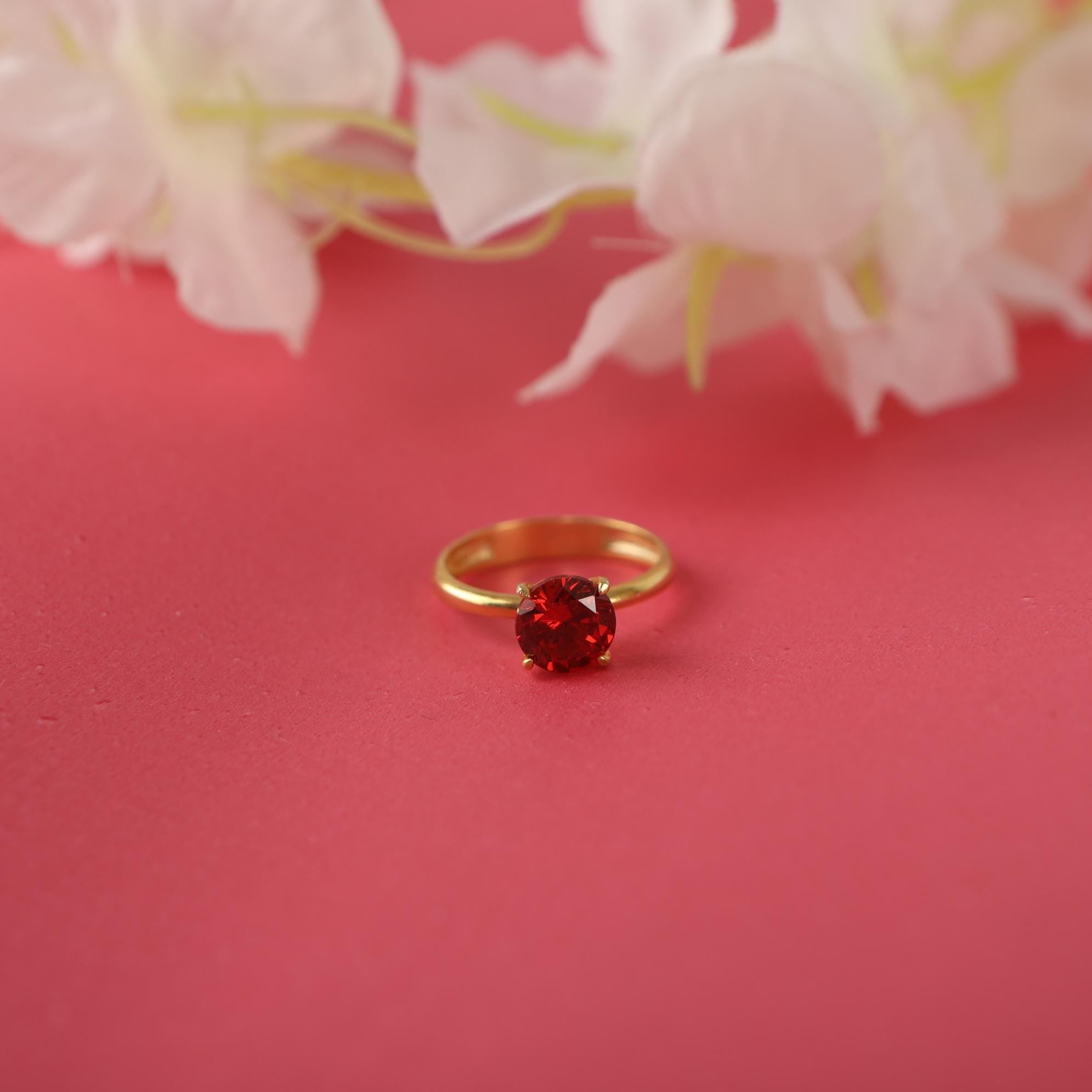 Gold ring with a red gemstone on a pink background with white flowers