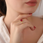 Close-up of a person wearing a gold ring with a red gemstone, holding their chin.
