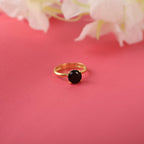 Gold ring with a black gemstone on a pink background with white flowers.