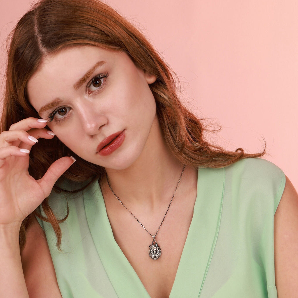 Woman wearing a green top and necklace against a pink background