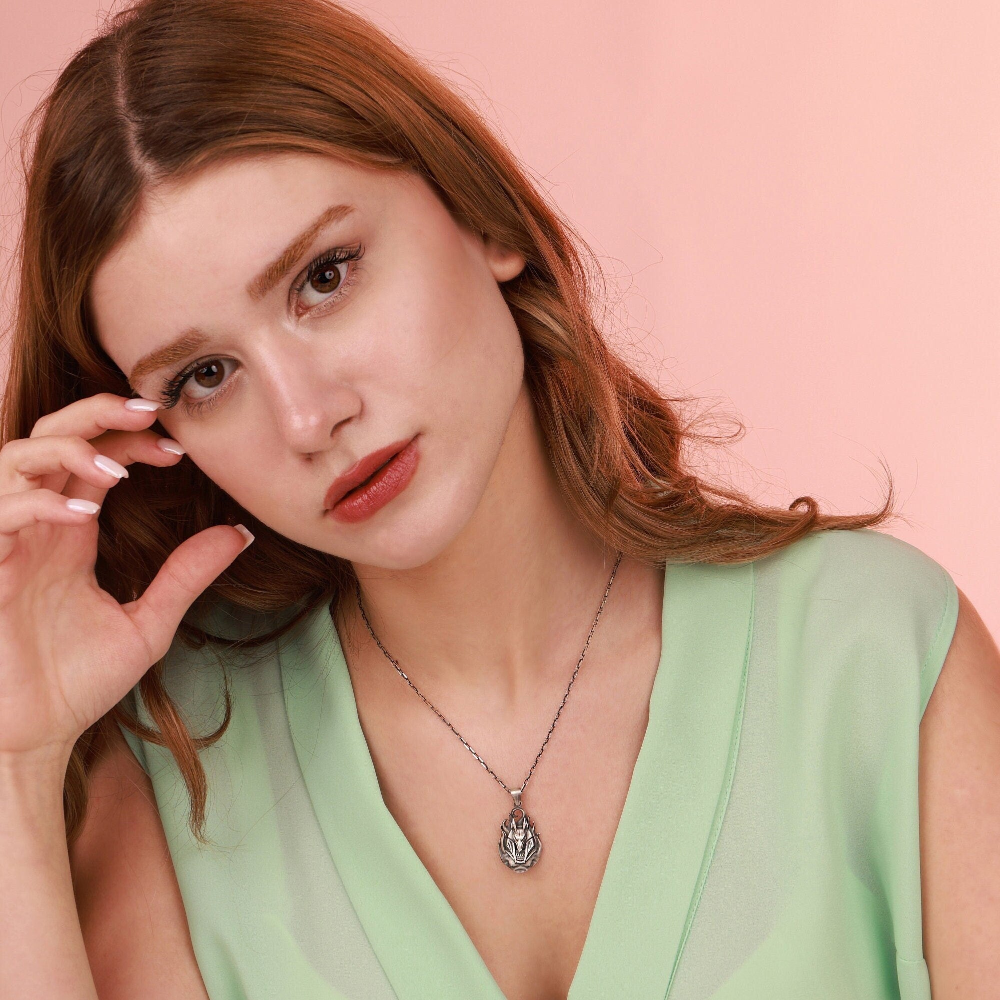 Woman wearing a green top and necklace against a pink background