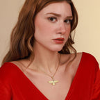 Woman wearing a red top and gold necklace with a pendant against a beige background