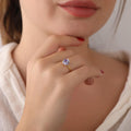 Close-up of a hand wearing a ring with a diamond, held near the chin.