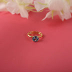Gold ring with a blue gemstone on a red background with white flowers