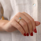 Close-up of a hand wearing a gold ring with gemstones against a neutral background