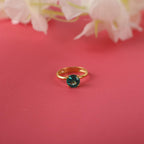 Gold ring with a green gemstone on a pink background with white flowers.