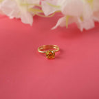 Gold ring with a orange gemstone on a pink background with white flowers.