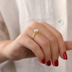 Close-up of a hand wearing a gold ring with a diamond on a light background