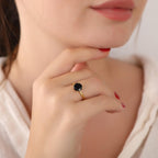 Close-up of a hand wearing a gold ring with a black gemstone, against a blurred background.