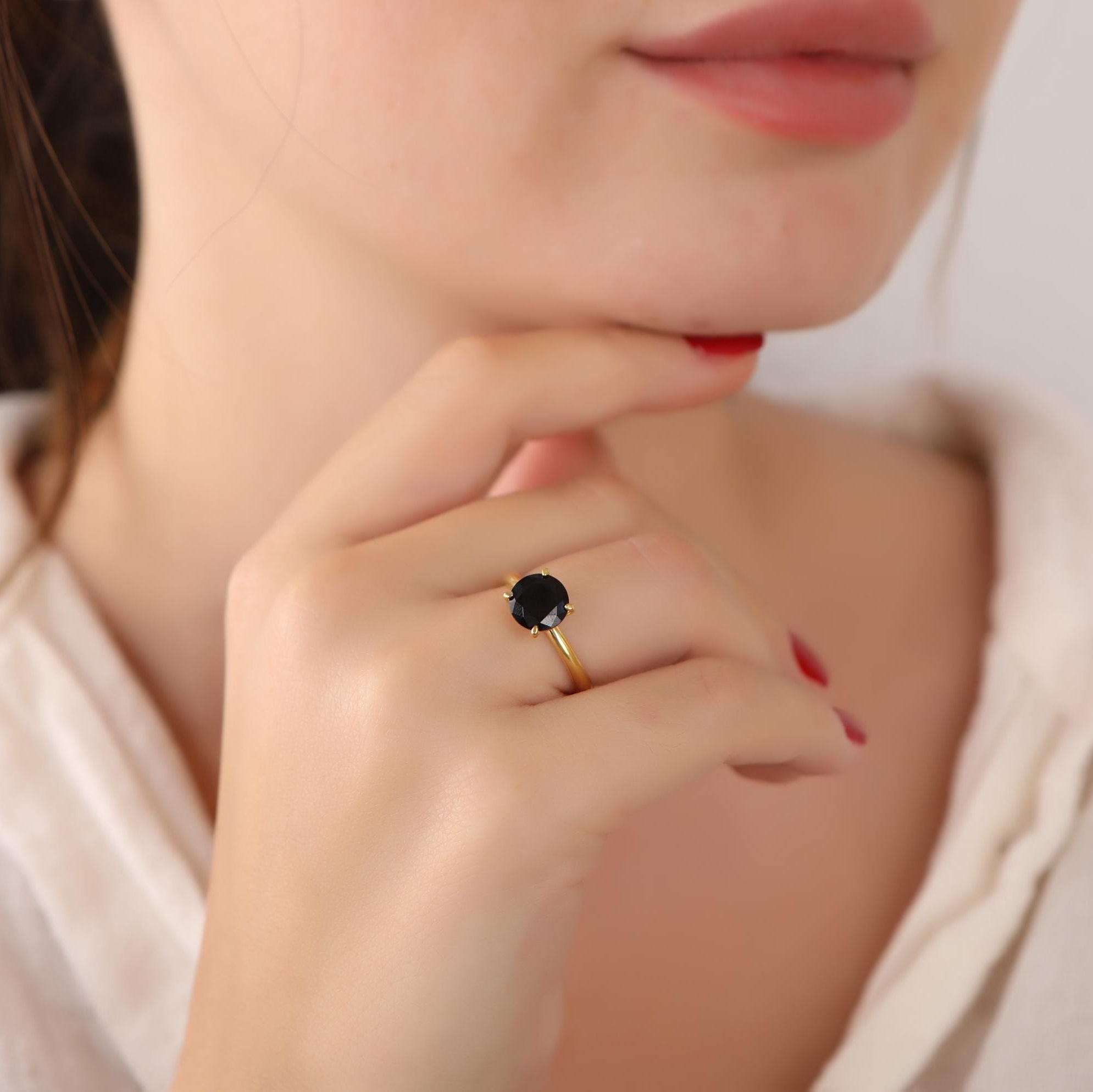 Close-up of a hand wearing a gold ring with a black gemstone, against a blurred background.