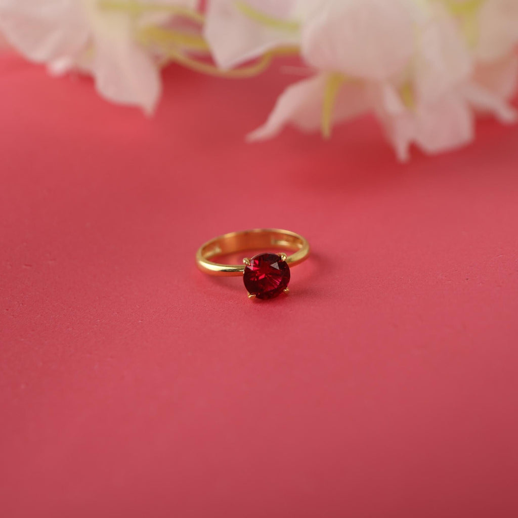 Gold ring with a red gemstone on a pink background with white flowers.