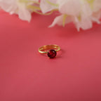 Gold ring with a red gemstone on a pink background with white flowers.