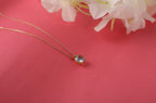Gold necklace with a blue gemstone pendant on a pink background