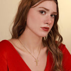 Woman wearing a red top and a gold vermeil necklace with a catholic cross pendant against a beige background