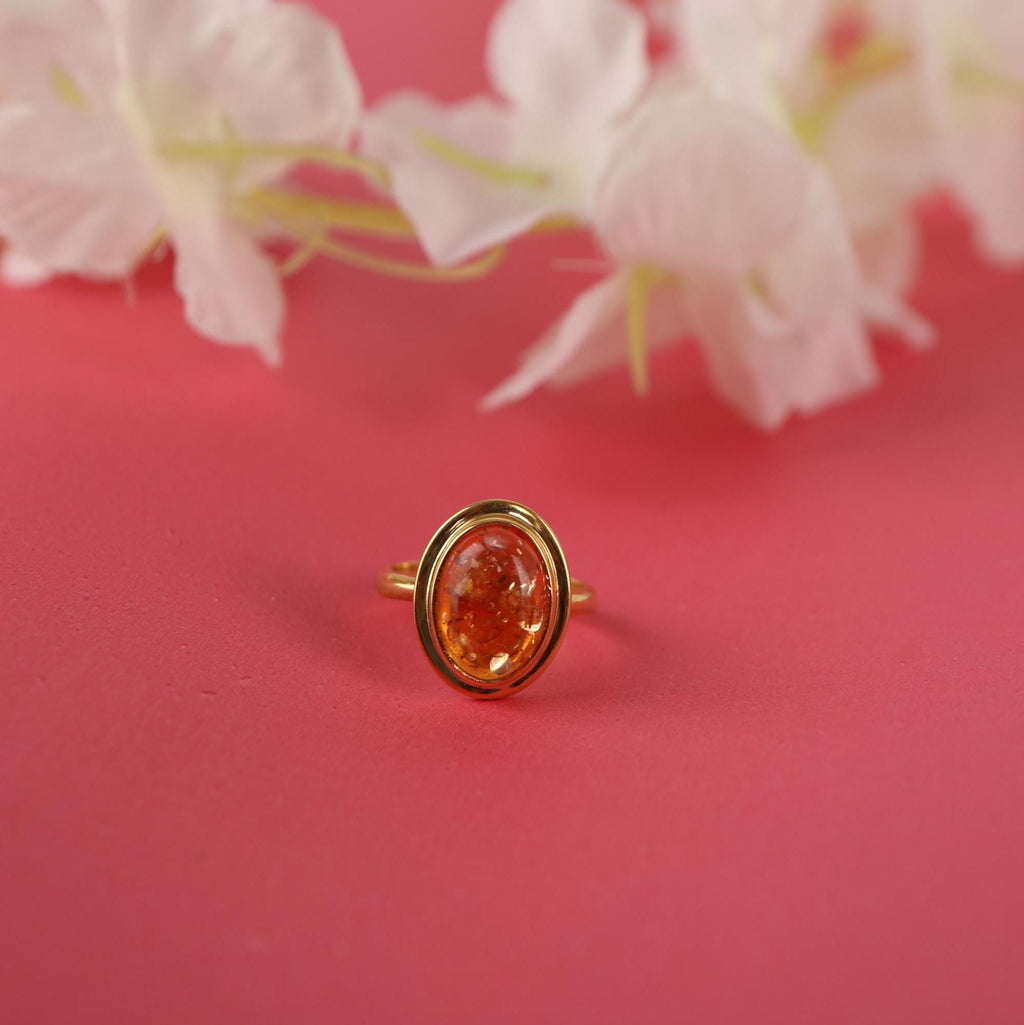 Gold ring with a orange gemstone on a pink background with white flowers