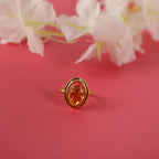 Gold ring with a orange gemstone on a pink background with white flowers