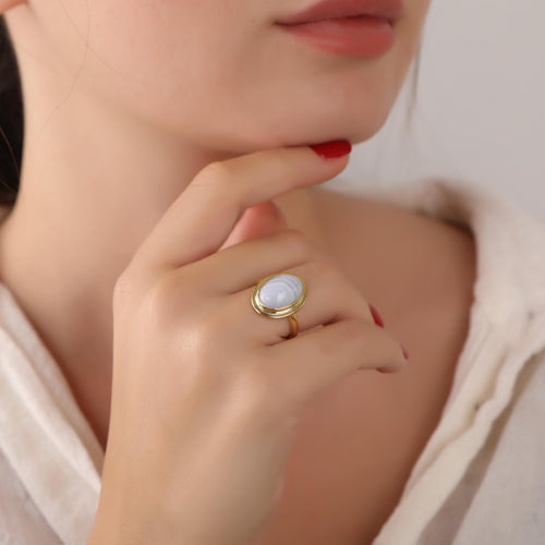 Close-up of a hand wearing a gold ring with a blue lace agate gemstone, touching the chin.