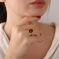 Close-up of a hand wearing a gold ring with a carnelian stone, touching the chin.