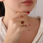 Close-up of a hand wearing a gold ring with a carnelian stone, touching the chin.