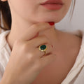 Close-up of a hand wearing a gold ring with a green agate gemstone, touching the chin.