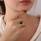 Close-up of a hand wearing a gold ring with a green agate gemstone, touching the chin.