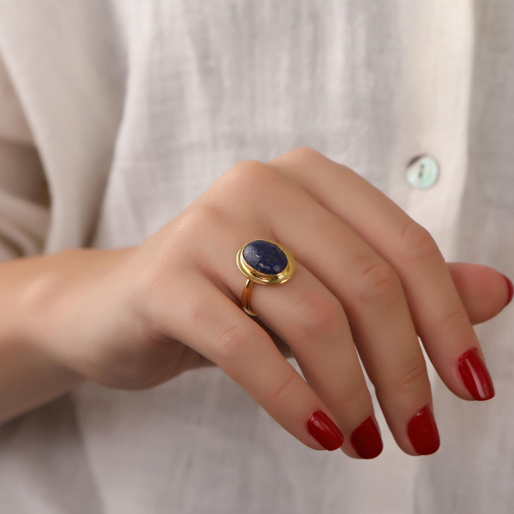 Hand wearing a gold ring with a blue stone against a neutral background