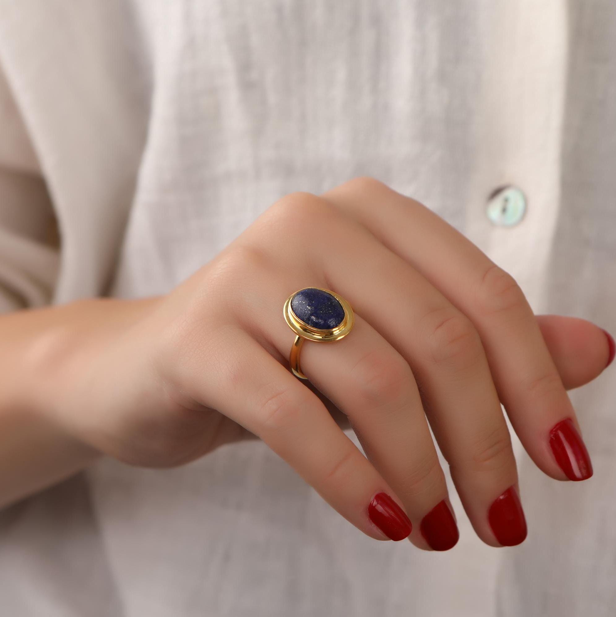 Hand wearing a gold ring with a blue stone against a neutral background