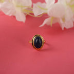 Gold ring with a dark stone on a pink background with flowers