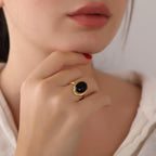 Close-up of a person wearing a gold ring with a black gemstone, touching their lips.