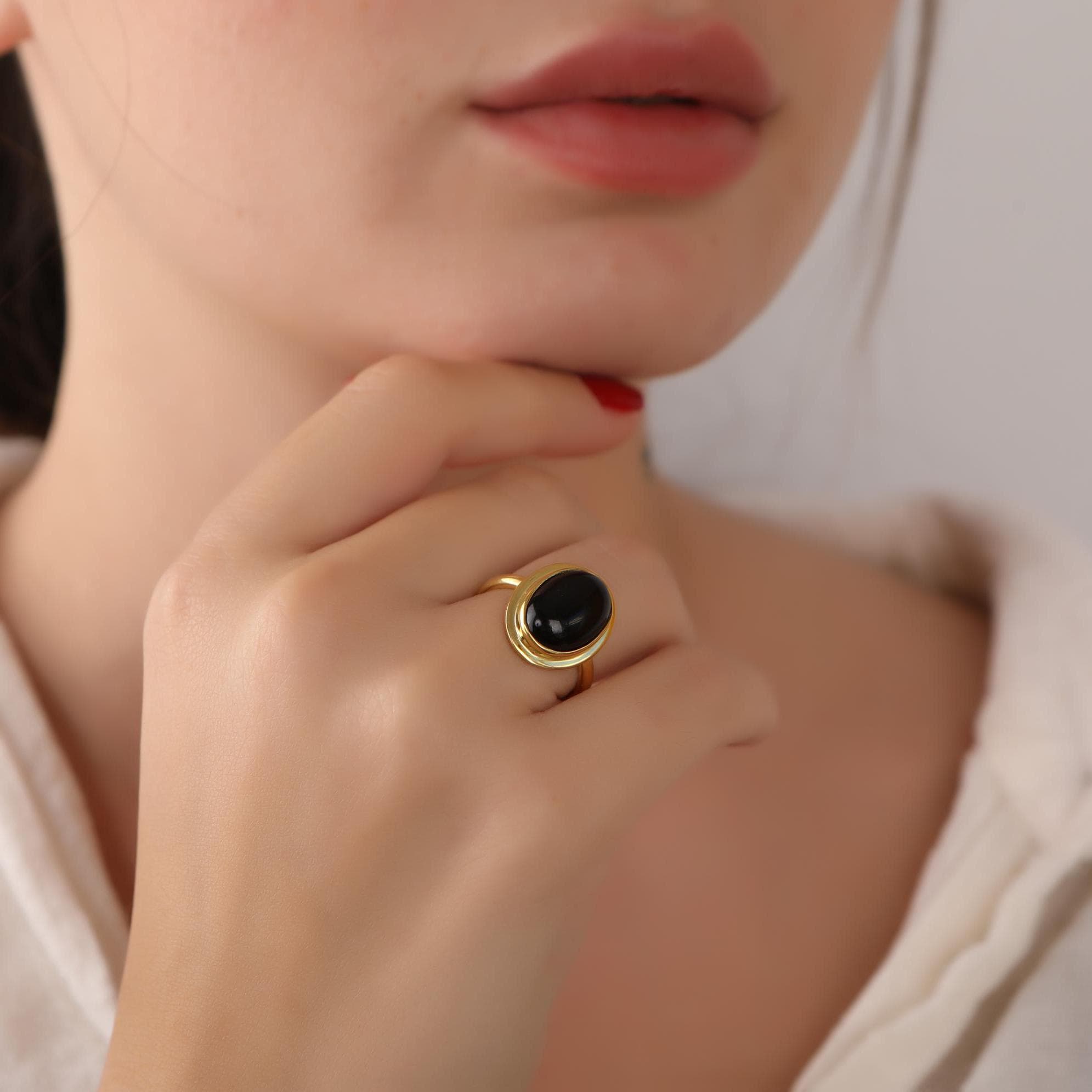 Close-up of a person wearing a gold ring with a black gemstone, touching their lips.