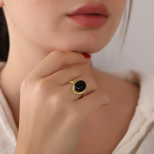 Close-up of a person wearing a gold ring with a black gemstone, touching their lips.