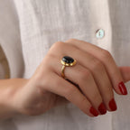 Hand wearing a gold ring with a black onyx against a neutral background