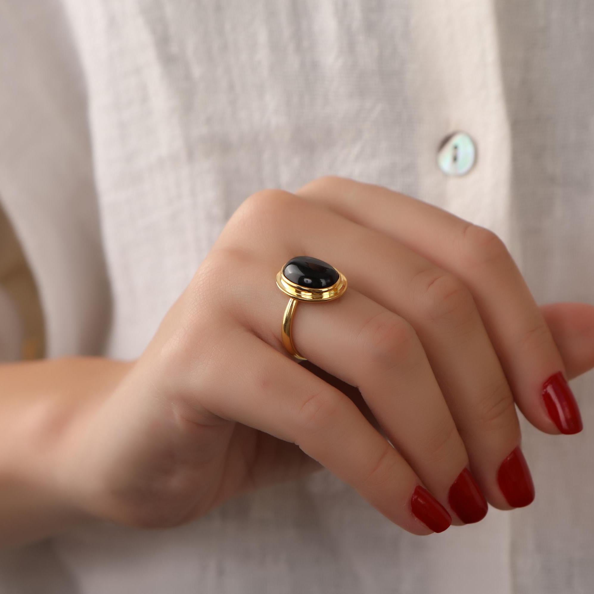 Hand wearing a gold ring with a black onyx against a neutral background