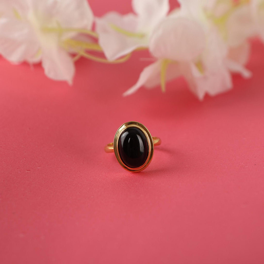 Gold ring with a black stone on a pink background with white flowers