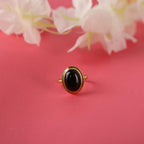 Gold ring with a black stone on a pink background with white flowers