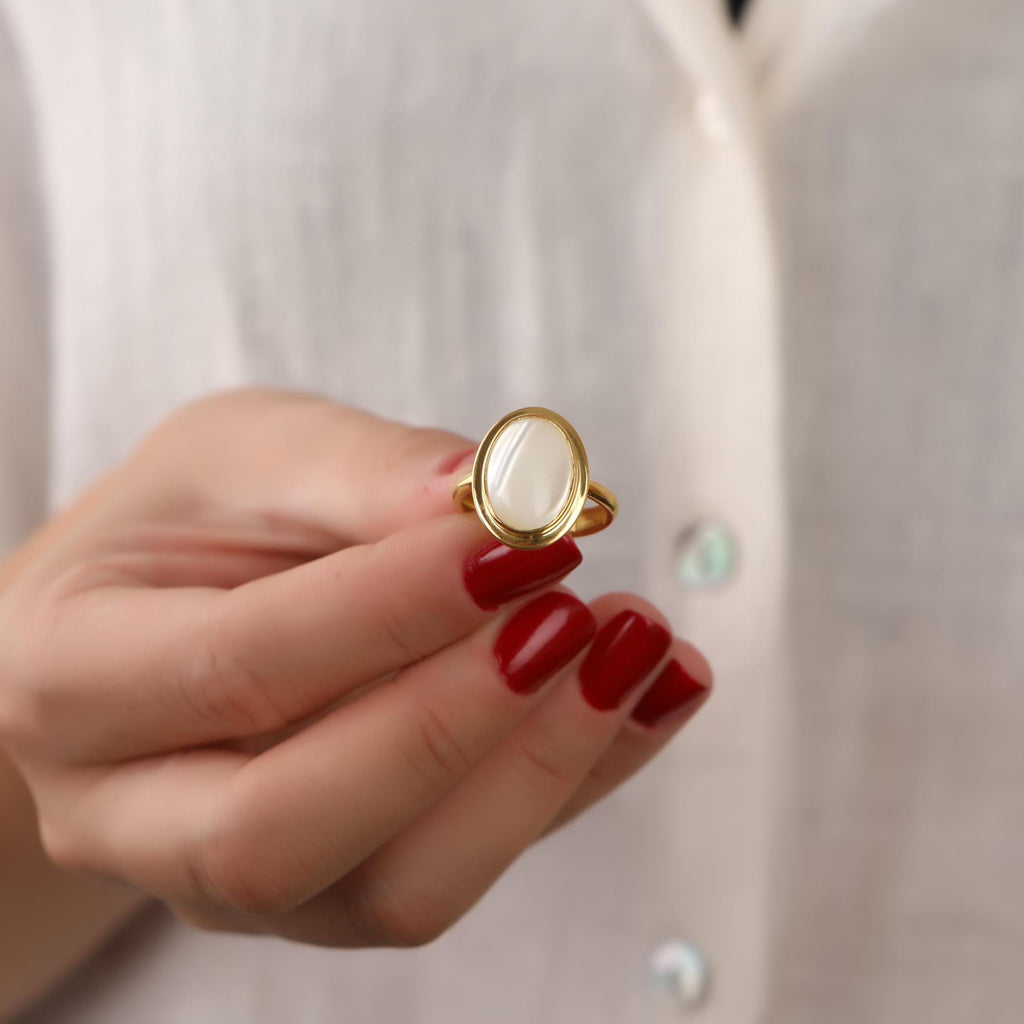 Hand wearing a gold ring with a white stone against a neutral background