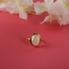 Gold ring with a pink stone on a red background with white flowers