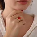 Close-up of a hand wearing a gold ring with a red stone, touching the chin.