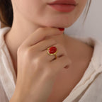 Close-up of a hand wearing a gold ring with a red stone, touching the chin.
